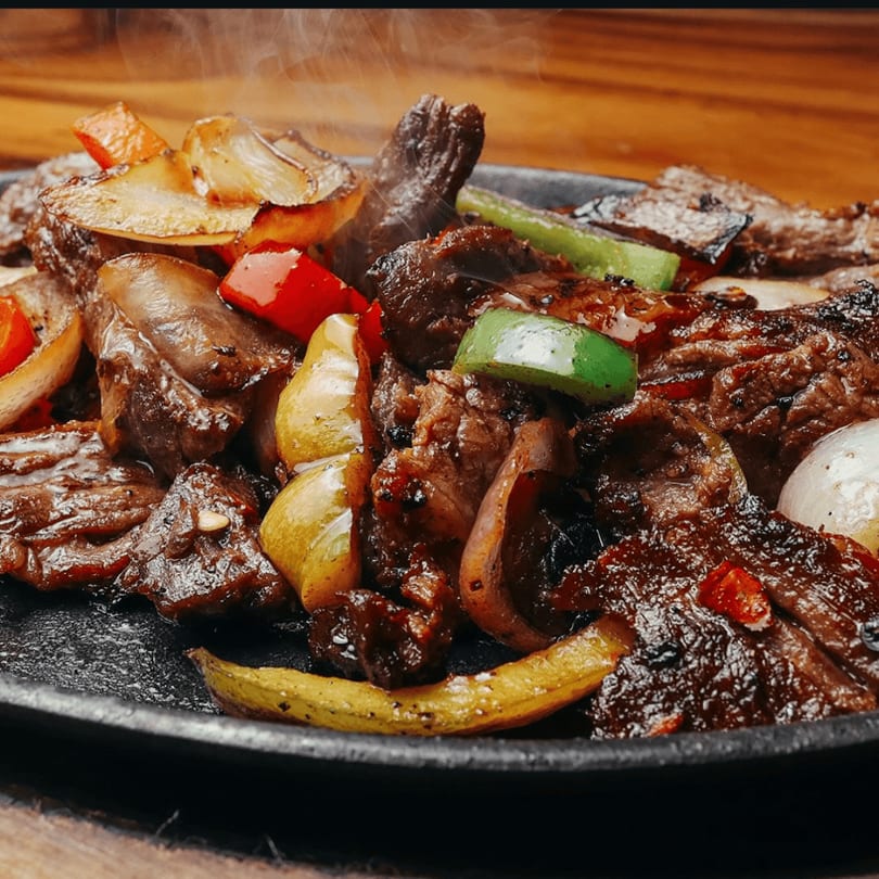 Sizzling steak fajitas with colorful bell peppers and onions on a hot cast iron plate.