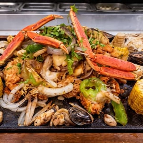 A large platter of seafood, including crab legs, mussels, corn, and vegetables, on a dark surface.