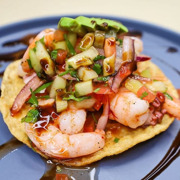 Shrimp and octopus ceviche tostada topped with avocado, cucumber, and a dark sauce.