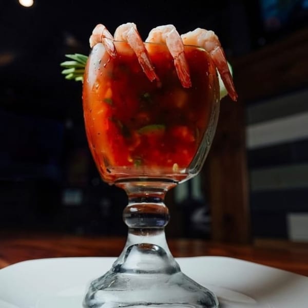 Shrimp cocktail in a large glass with red sauce and a garnish on a white plate.