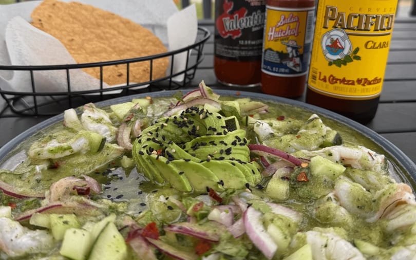 Aguachile with shrimp, avocado, red onion, and cucumber, served with tostadas, hot sauce, and beer.