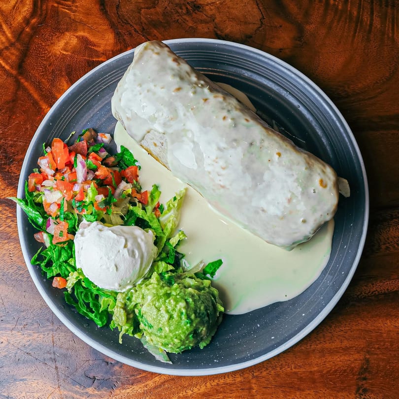 A large, white-sauced burrito with a side of guacamole, sour cream, and pico de gallo.