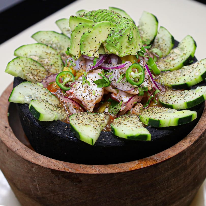 Mexican seafood ceviche with avocado, cucumber, and jalapeños in a dark stone bowl.