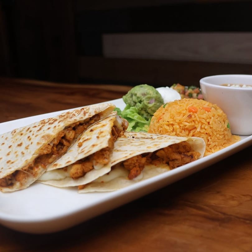 Chicken quesadillas with rice, guacamole, and a side of soup on a white plate.