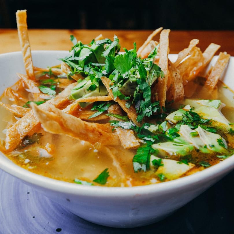 Close-up of a bowl of Mexican tortilla soup with avocado, cilantro, and crispy tortilla strips.