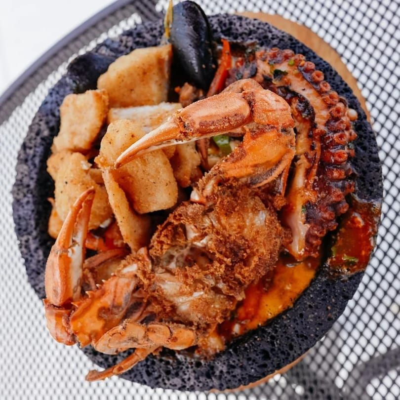 A molcajete filled with fried fish, crab, octopus, and mussels in a red sauce.